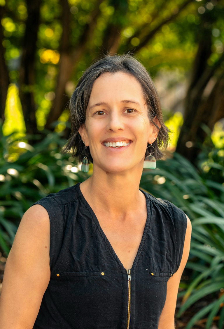 Dr Jackie Gould smiling in front of dark green trees in the chinese garden