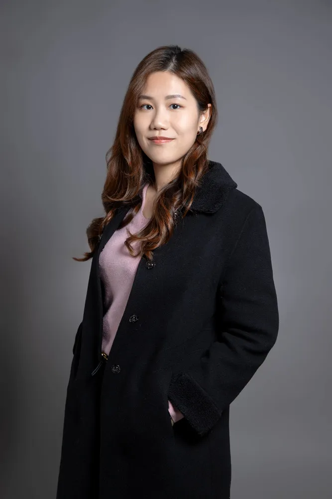 Woman wearing dark coat and pink shirt smiling at camera