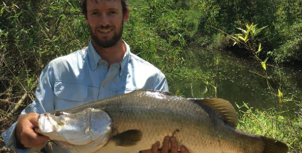 man holding large fish with water and dense vegetation in background