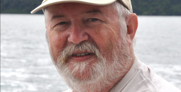 Dr Julian Pepperell head and shoulders, wearing cap, with water and forest in background