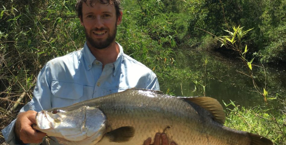 Brien Roberts holding a large fish, with bush and waterway in background