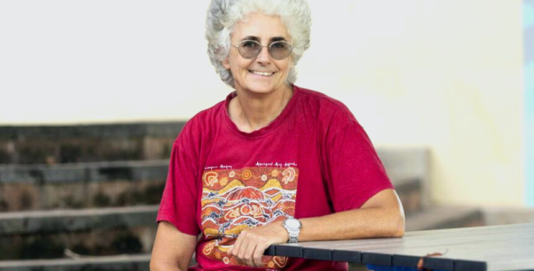 Researcher & Lecturer Cat Kutay sitting down on table with red shirt