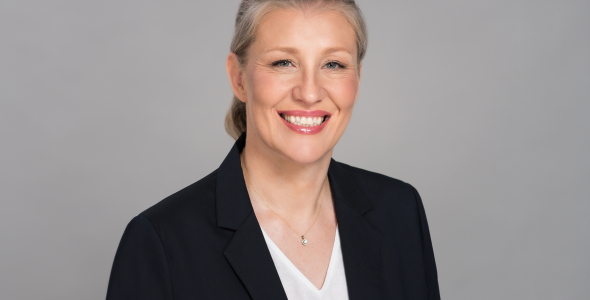 Woman with black jacket, blonde hair, blue eyes, smiling towards camera