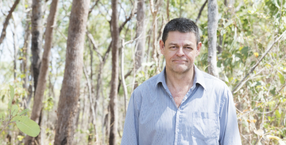 Lindsay Hutley, head to waist, wearing a blue shirt, with trees and shrubs in the background