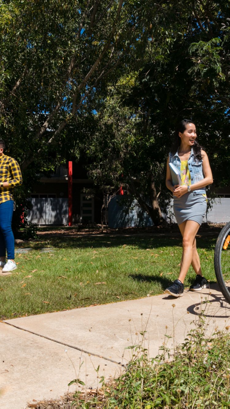 Two female students walking their bikes and smiling