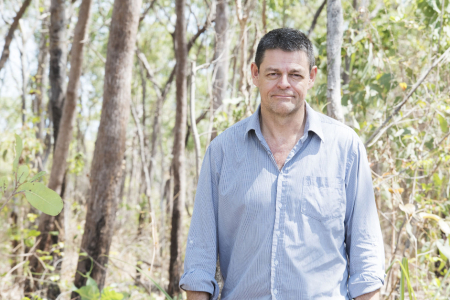 Lindsay Hutley, head to waist, wearing a blue shirt, with trees and shrubs in the background