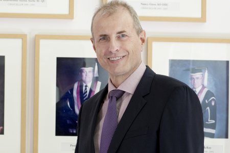 Image of Caucasian man wearing black suit jacket and purple tie. 