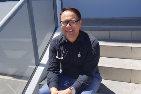 Man sitting on stairs smiling with stethoscope around his neck. 