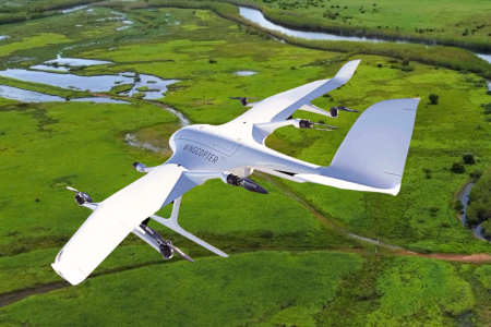 Fixed-wing uncrewed aerial vehicle, with "Wincopter" written on it, flying over lush green country with wetlands and river in background