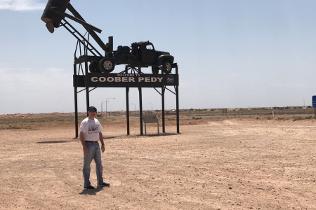 man stands in front of sign in outback