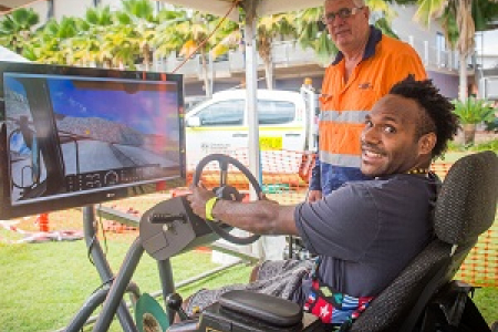 Jerimus Dimpamala tests his skills at the new dump truck simulator at CDU Open Day. Pictured with VET lecturer Peter Bacon