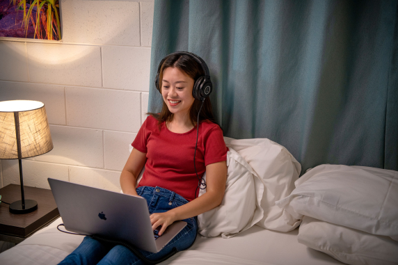 Female student smiling and looking at laptop while wearing headphones