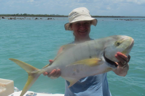 person wearing hat, standing in boat, holding large fish, with water in the background