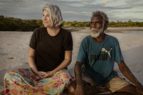 researchers jen and paul sit on beach and look out onto sunset