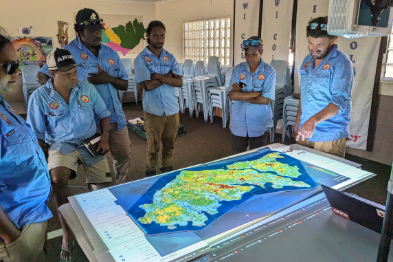 Tiwi Rangers stand around table looking at 3D topographical map of fire simulations over the islands