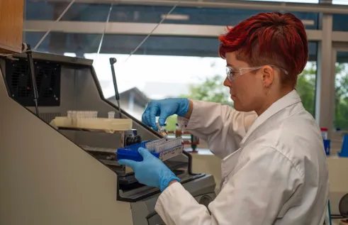 Dr Alea Rose in a laboratory, holding a test tube and a blue rack of test tubes