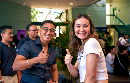 Two people posing with thumbs up. One person in dark button up shirt and another person in short sleeve white shirt.