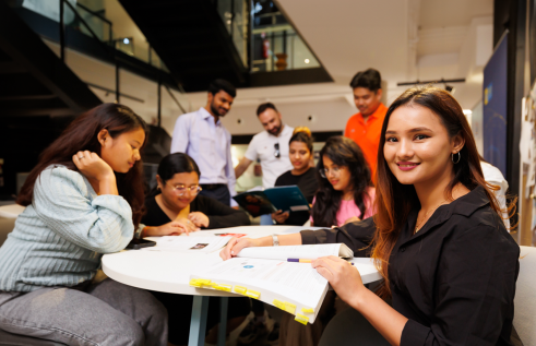 Group of students sitting and standing around a table.