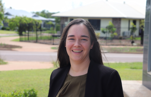 Dr Ingrid Conninx, head and shoulders, wearing black jacket and brown blouse, with green lawn, road and houses out of focus in background