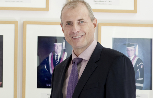 Image of Caucasian man wearing black suit jacket and purple tie. 