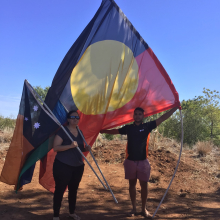 Luke standing outdoors raising a large Aboriginal flag