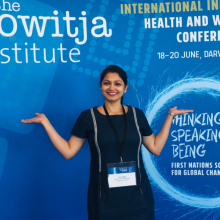 Athira smiling in front of a promotion for the International Indigenous health and Wellbeing Conference 2019