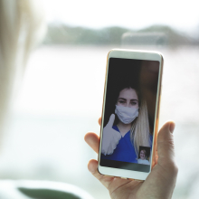 Stock image of a nurse in PPE talking to someone via telehealth or video confernece