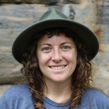 Jennifer Macdonald head and shoulders, wearing hat, with stone wall in background