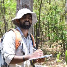 Man standing in forest writing in notebook