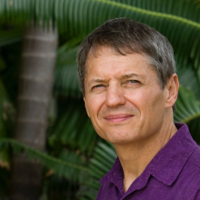 Keith Christian head and shoulders with palm tree trunk and large green leaves in the background