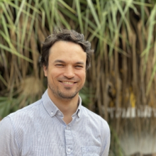 Dr Clement Duvert, head and shoulders, with green spiky-looking leaves hanging down in background