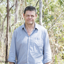 Lindsay Hutley, head to waist, wearing a blue shirt, with trees and shrubs in the background