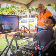 Jerimus Dimpamala tests his skills at the new dump truck simulator at CDU Open Day. Pictured with VET lecturer Peter Bacon