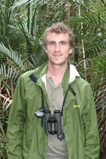 Simon Mahood with binoculars around his neck and palms in the background
