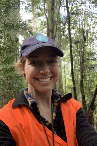 Anna Richards wearing CSIRO cap and high vis vest, with tall trees in background